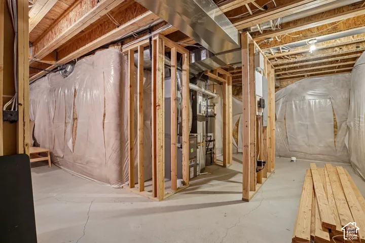 Unfinished basement space with exposed wooden joists and framing, a concrete floor, and visible utility systems including ductwork and electrical wiring