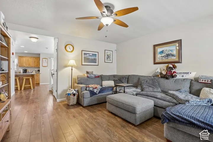 Spacious living area featuring wood-finish flooring, a ceiling fan with integrated lighting, and neutral wall tones