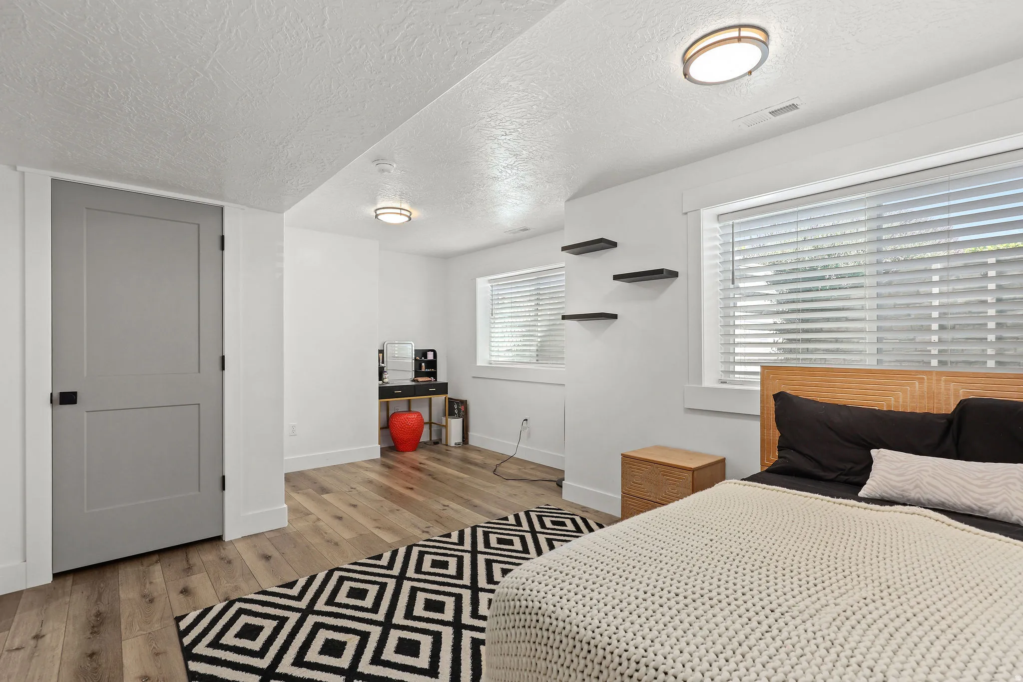 Spacious room featuring wood-finish flooring, bright white walls, and a recessed window with blinds