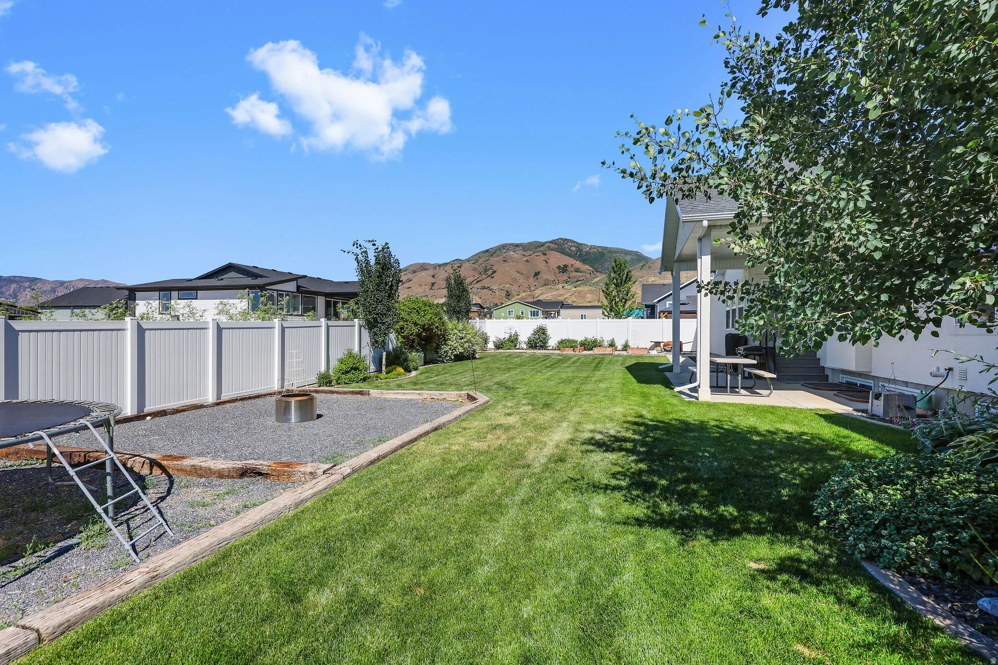 Expansive backyard featuring a manicured lawn, a dedicated gravel area with a fire pit, and a private patio space under a covered porch