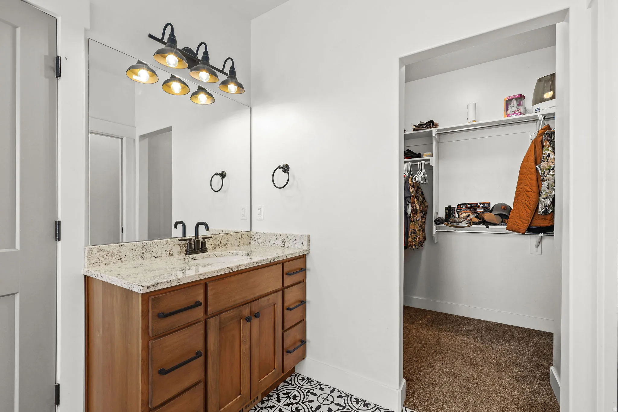 Bathroom vanity featuring a light-toned stone countertop, wood-finish cabinetry with dark hardware, and a framed mirror