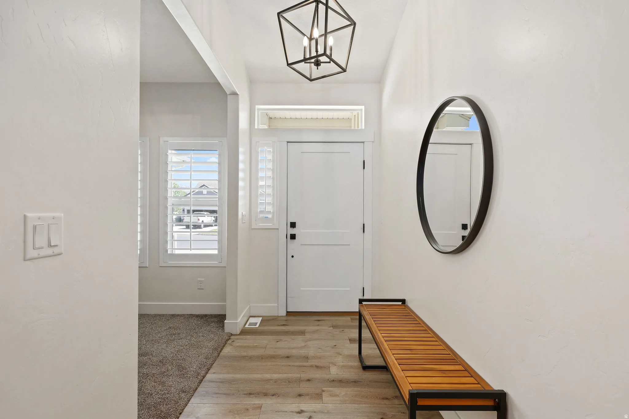 Entryway featuring wood-finish flooring, a contemporary chandelier, white paneled entry door, and side-light windows with plantation shutters