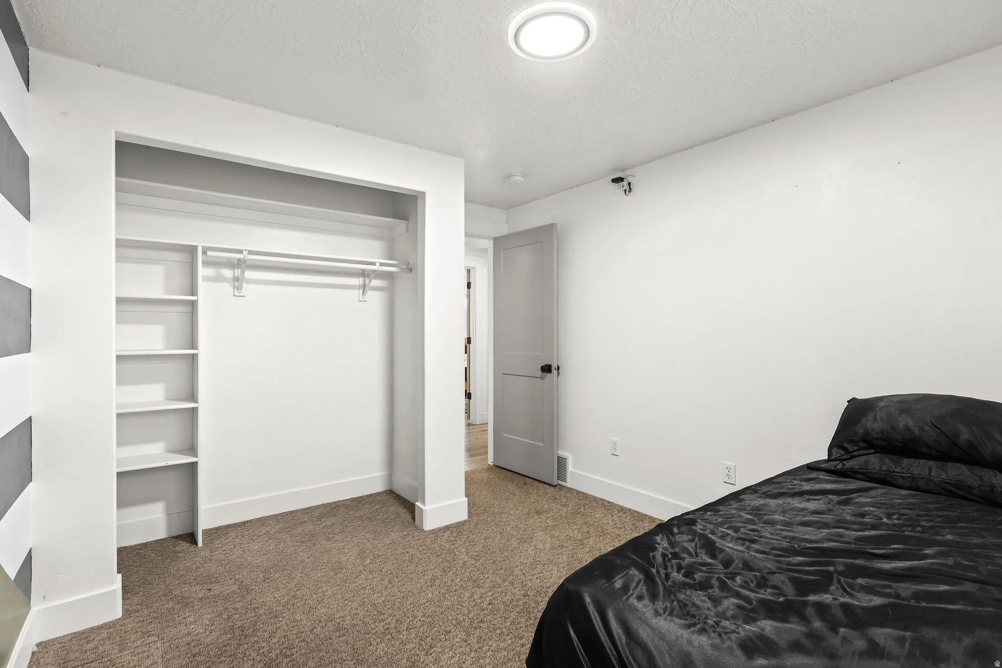 Carpeted room featuring a built-in closet with shelving and hanging rod, white walls, and a flush-mount ceiling light