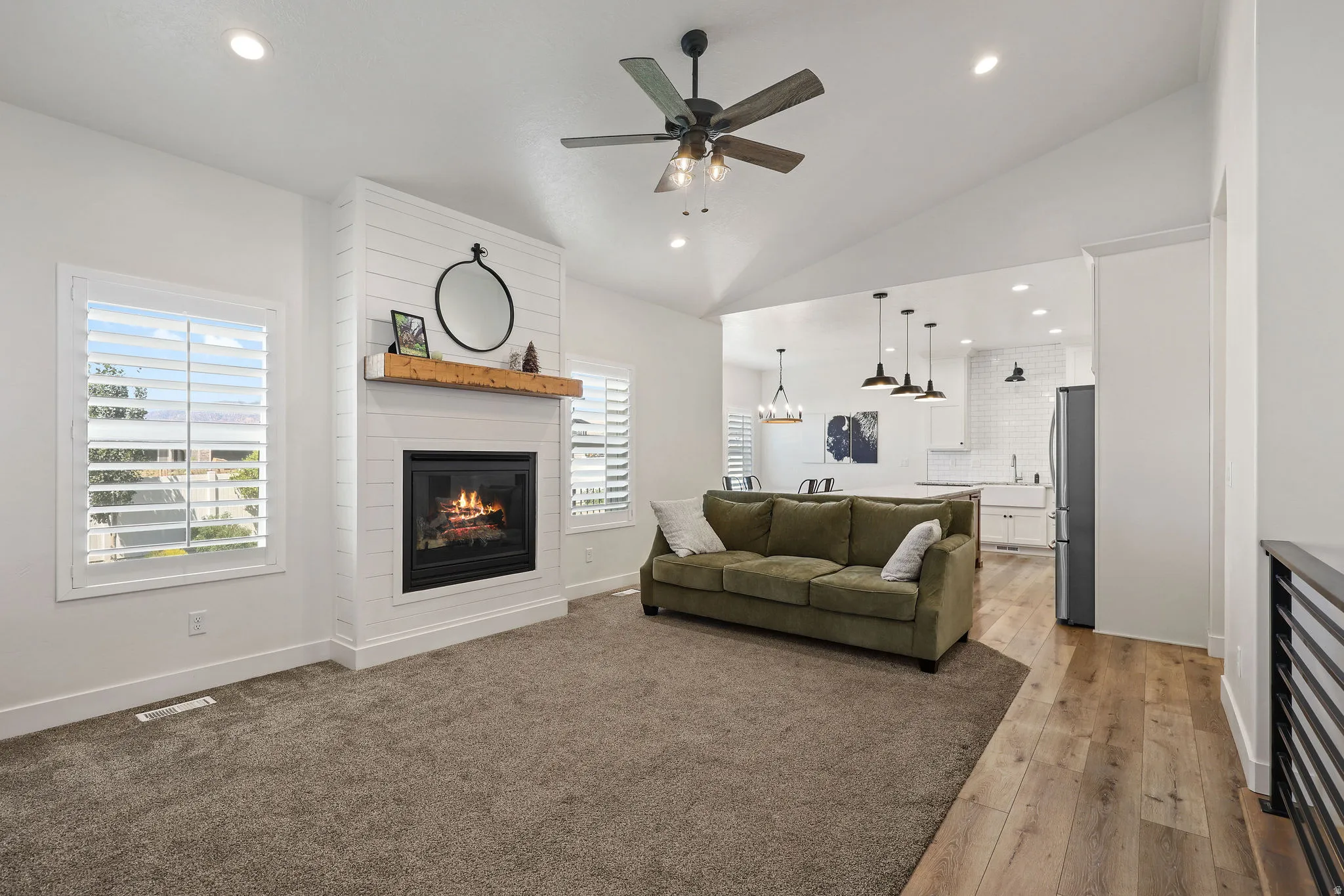 Spacious living area featuring a central fireplace with shiplap surround and wood mantel, vaulted ceiling, and recessed lighting