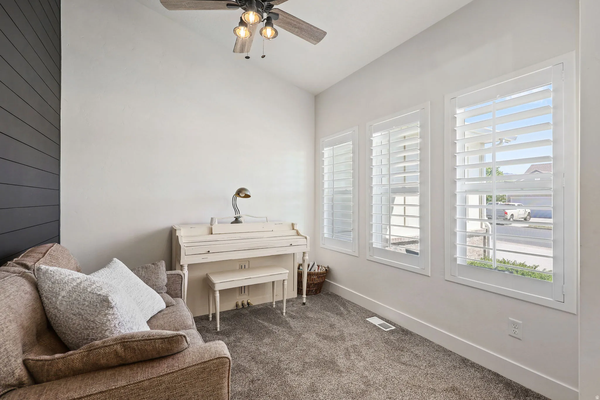Interior space featuring three windows with white plantation shutters, a dark shiplap accent wall, light gray walls, and textured gray carpeting