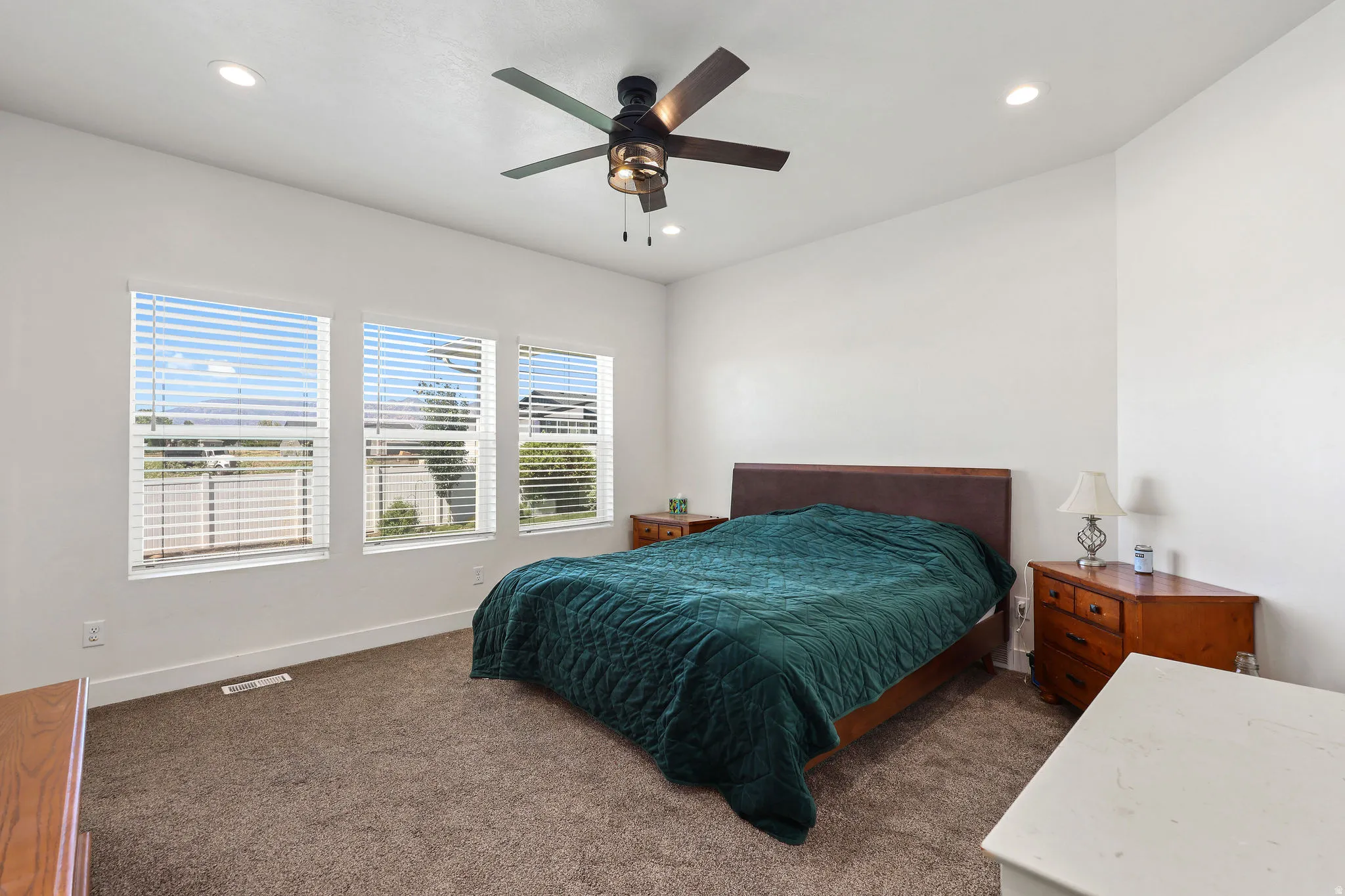Room featuring three rectangular windows with horizontal blinds, carpet flooring, a ceiling fan with integrated lighting, and recessed ceiling lights