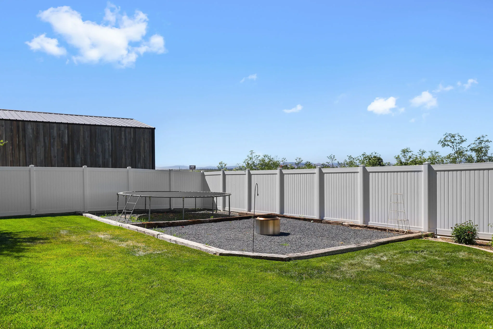 Expansive backyard featuring a manicured lawn, full privacy fencing, and a dedicated gravel area with a built-in fire pit