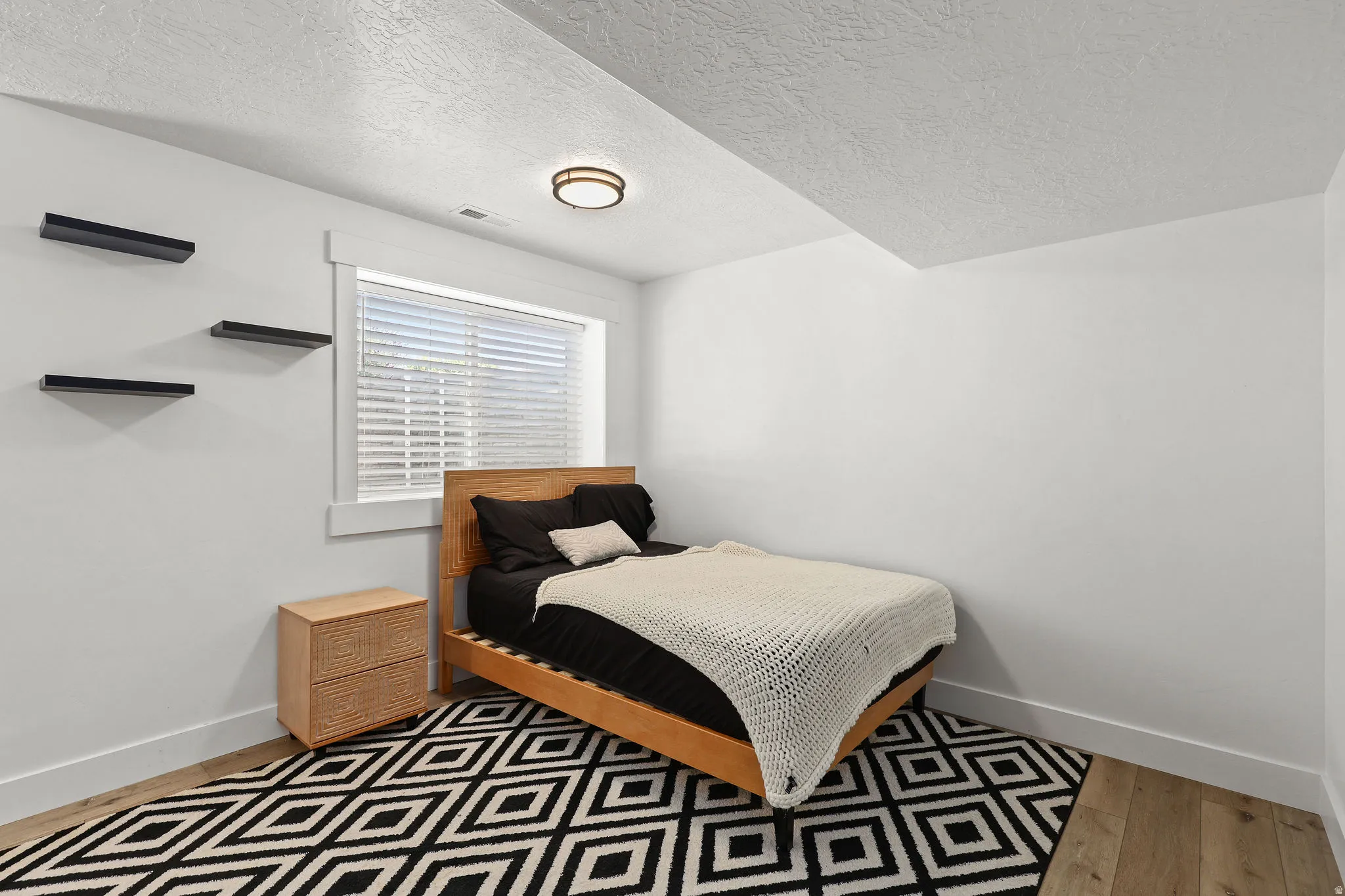 Bedroom featuring wood-finish flooring, a window with blinds, and white walls