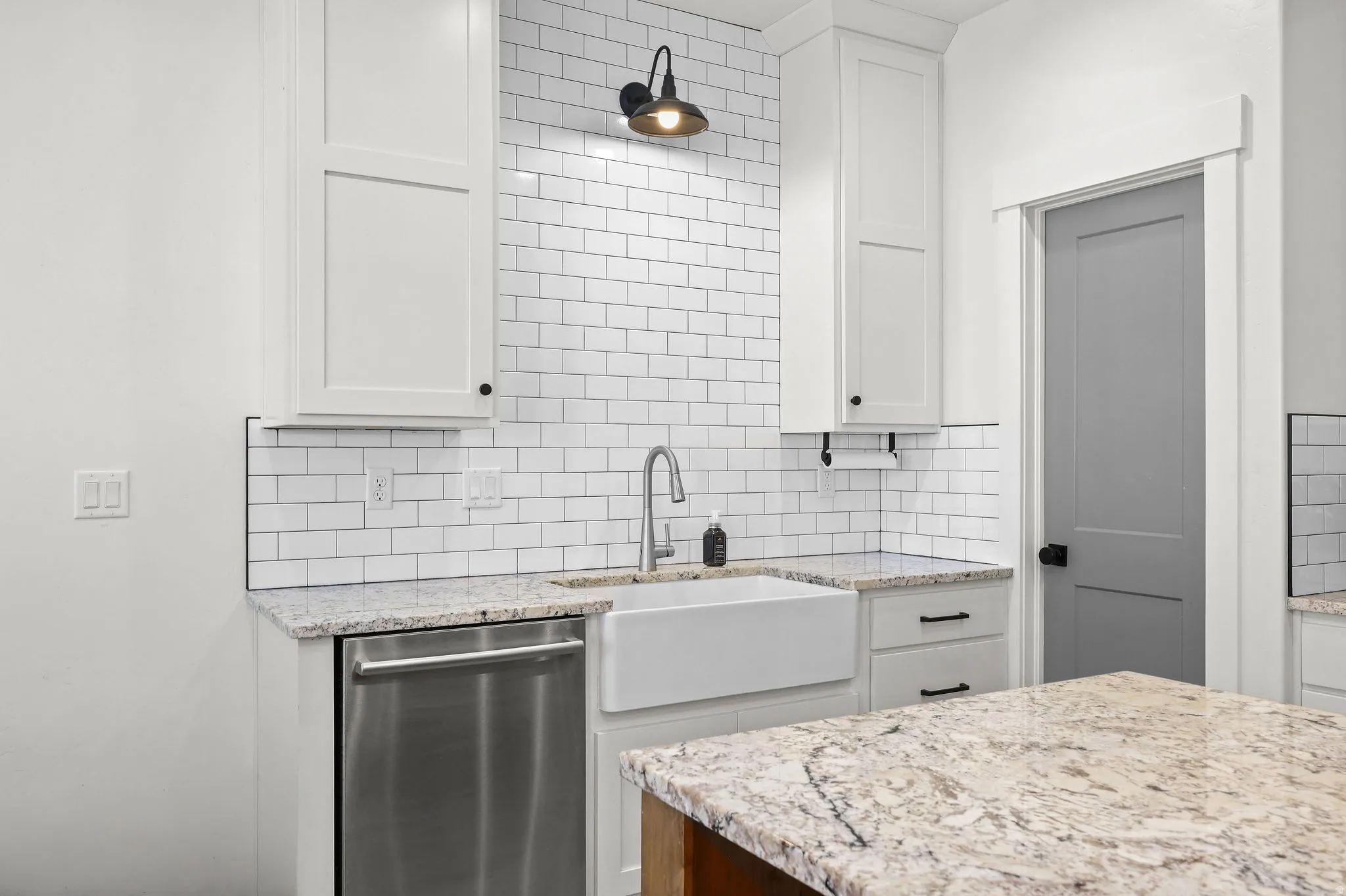 Modern kitchen featuring white shaker cabinetry, an apron-front sink, stainless steel dishwasher, and granite countertops