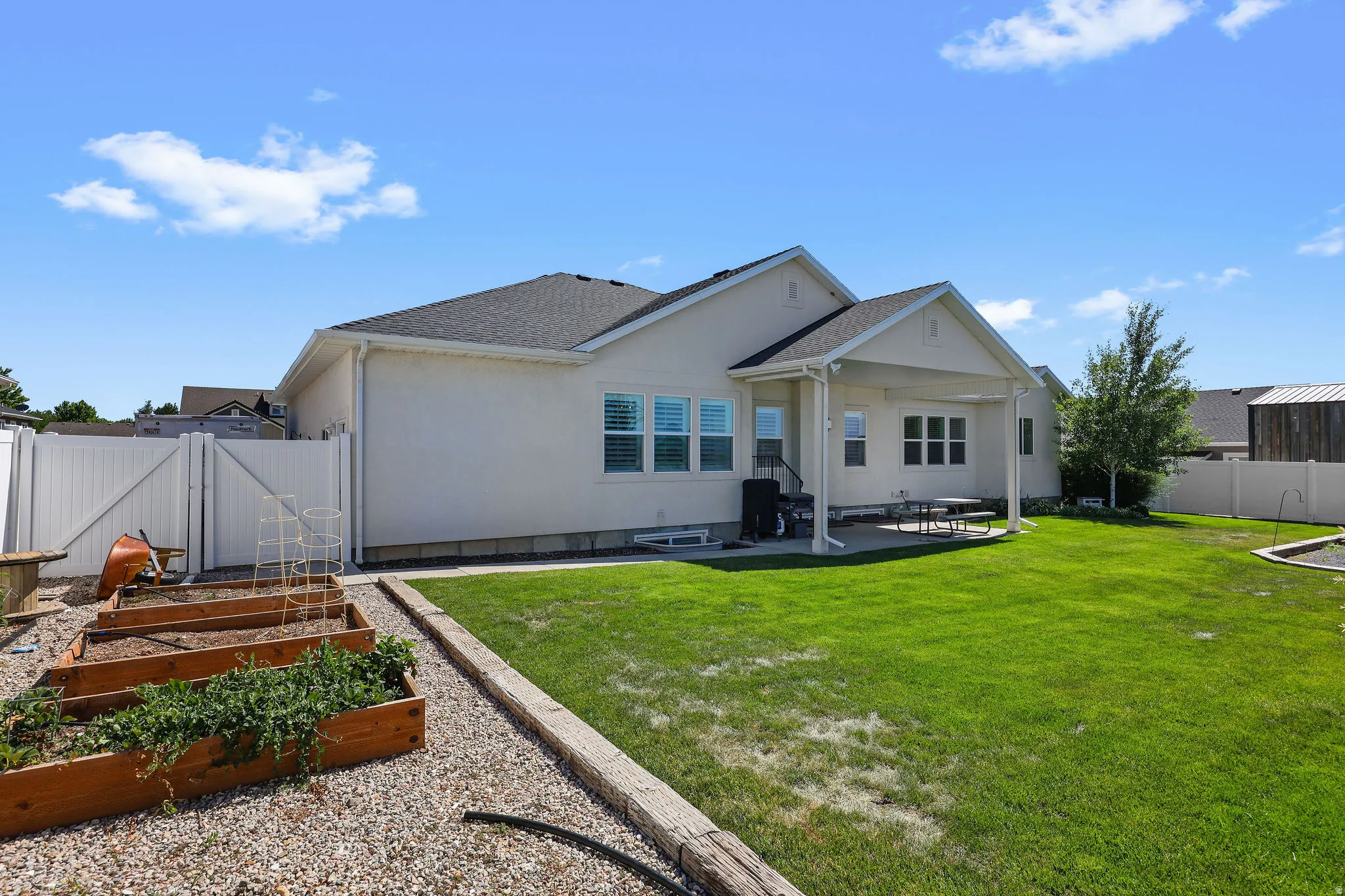 Expansive backyard featuring a manicured lawn, a covered patio, and raised garden beds