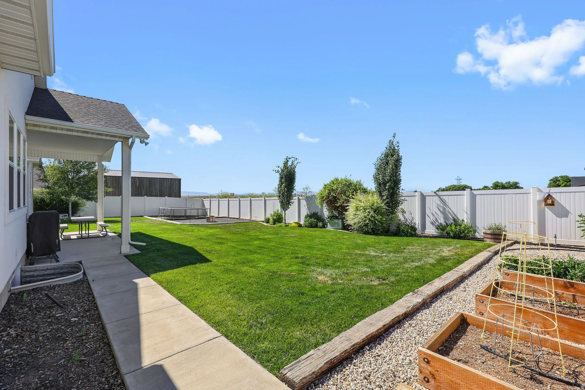 Expansive backyard featuring a covered patio, manicured lawn, raised garden beds, and a perimeter privacy fence