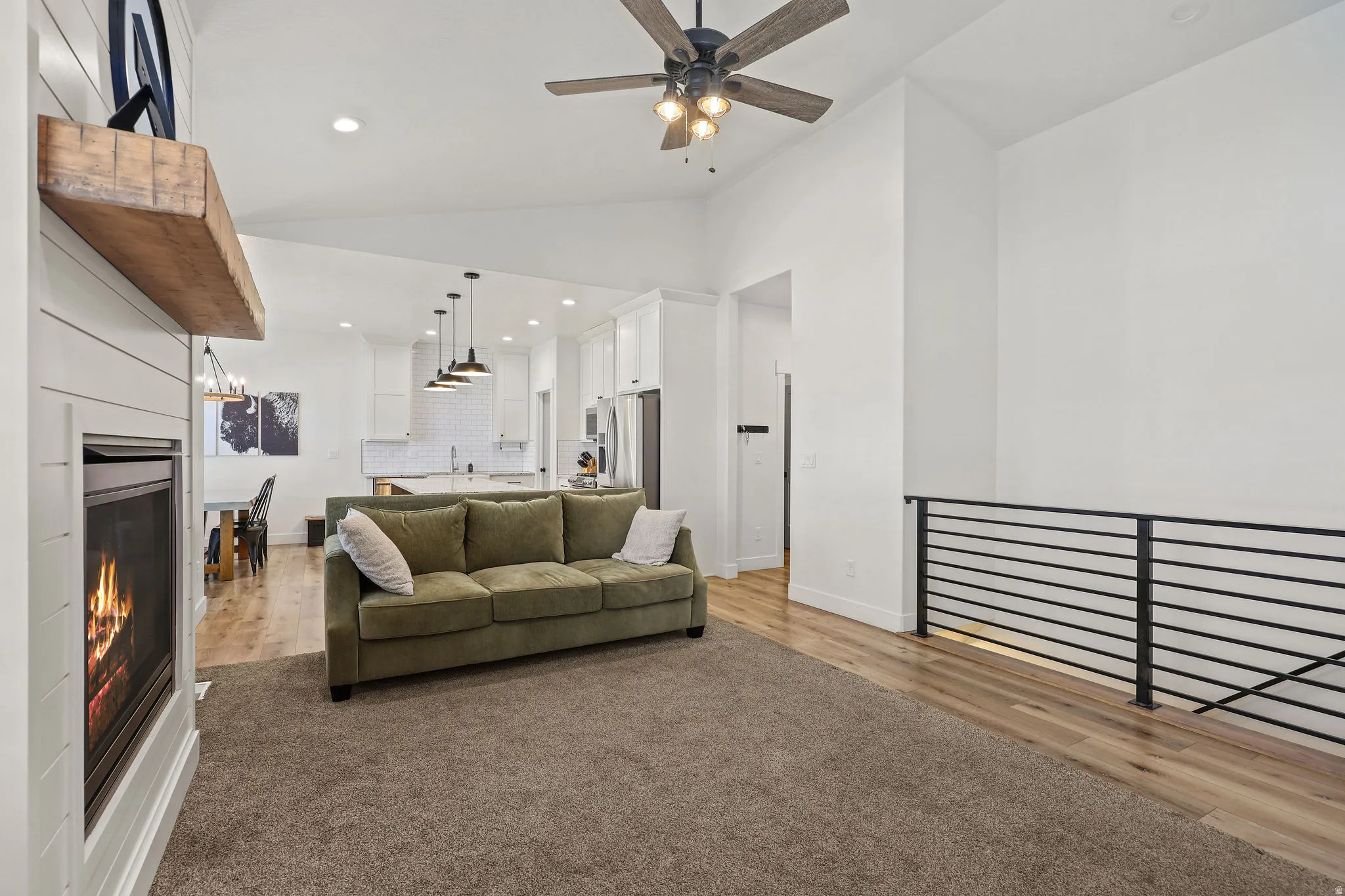 Living area featuring a shiplap fireplace with a wood-beam mantel, vaulted ceilings, and a ceiling fan