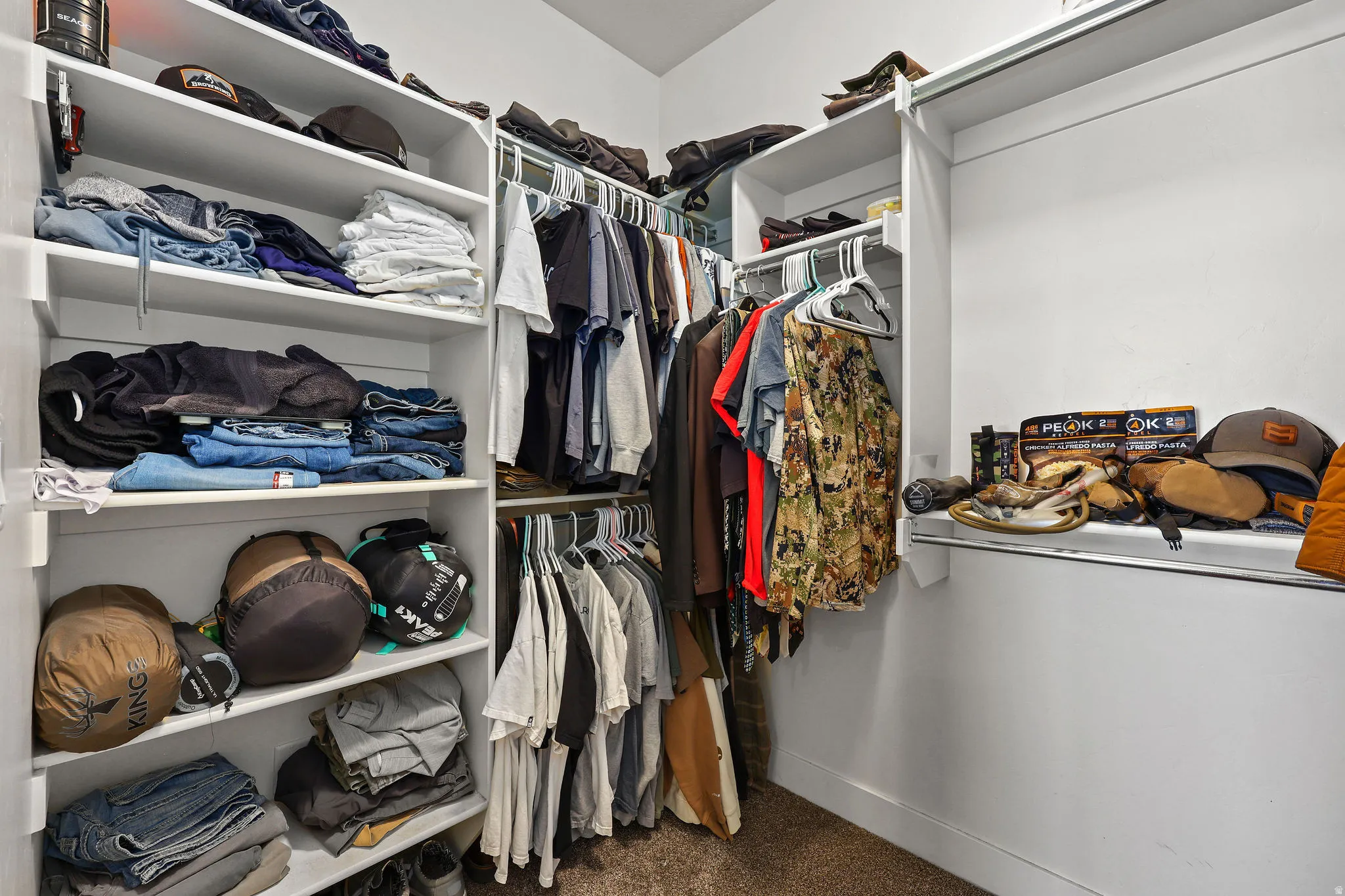 Walk-in closet featuring white built-in shelving, multiple hanging rods, and neutral-toned carpeting