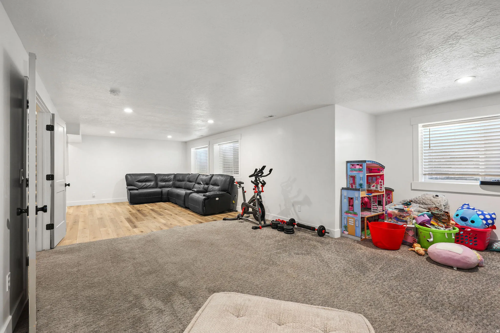 Spacious room featuring a combination of carpeted and wood-finish flooring, recessed lighting, and multiple windows with blinds