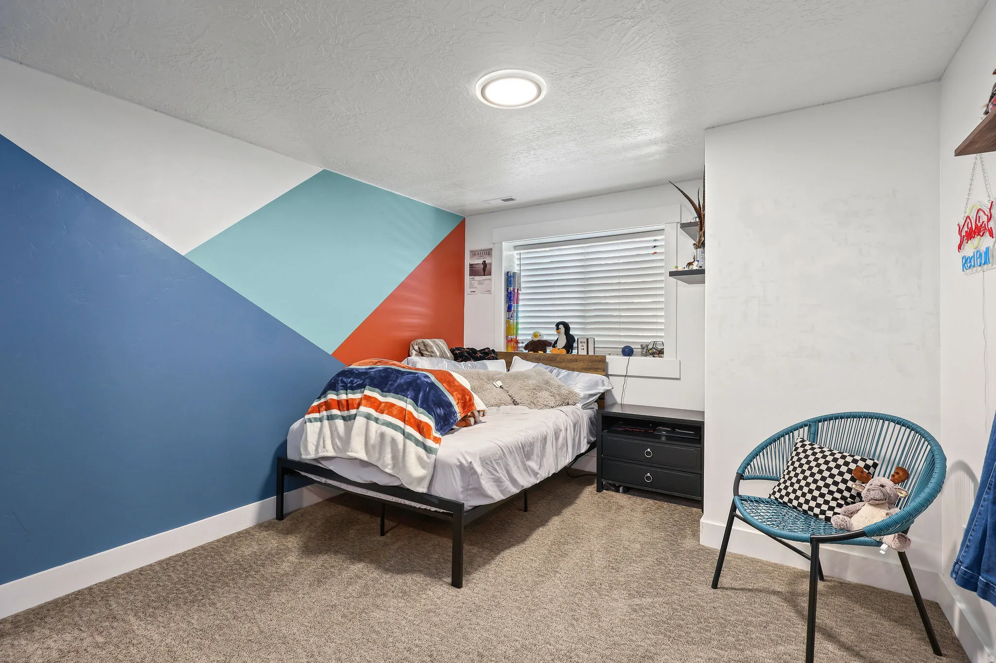 Carpeted room featuring a geometric accent wall with blue, turquoise, and orange hues