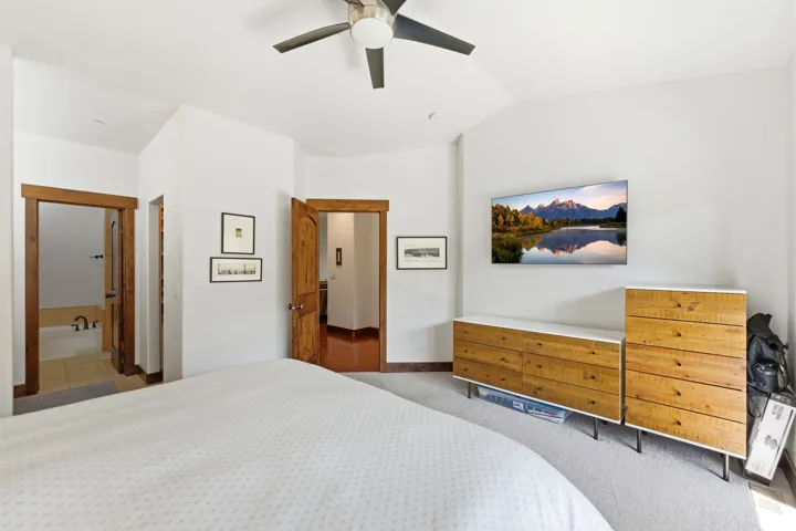 Carpeted bedroom featuring a ceiling fan, vaulted ceiling, and wood-trimmed doorways