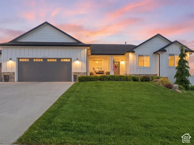 Contemporary farmhouse-style exterior featuring white board and batten siding, dark trim, a two-car garage with transom windows, a concrete driveway, and a manicured lawn