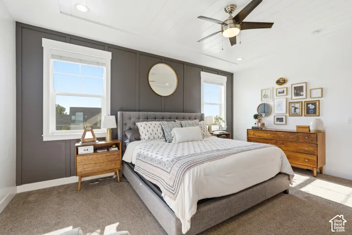 Bedroom featuring board and batten accent wall, two large windows, textured carpeting, a ceiling fan with integrated lighting, and recessed ceiling lights