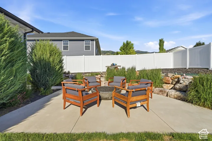 Concrete patio featuring a built-in fire pit, surrounded by tiered landscaping with natural rock elements and mature privacy shrubs