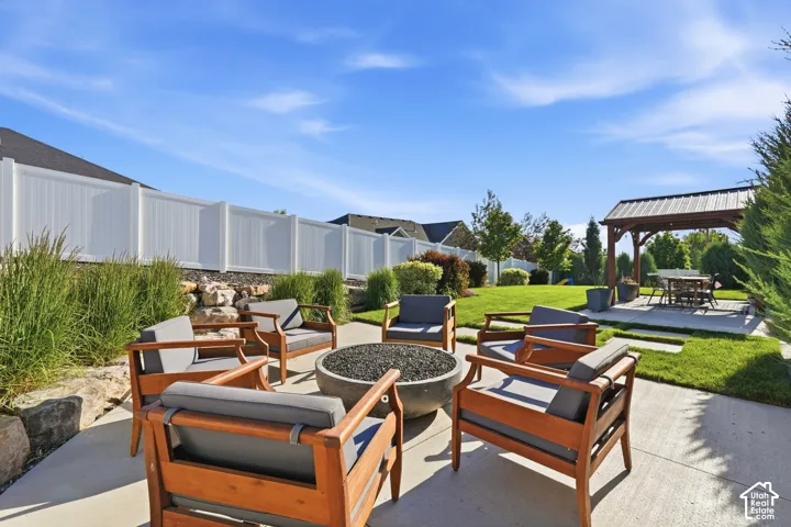 Expansive outdoor living area featuring a concrete patio with a built-in fire pit, a dedicated pergola-covered dining space, and a manicured lawn