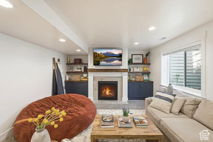 Living area featuring a gas fireplace with a stone surround, a wood mantel, and built-in cabinetry with open shelving