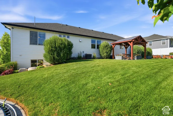 Expansive rear lawn featuring a wooden pergola with a built-in table and bench seating