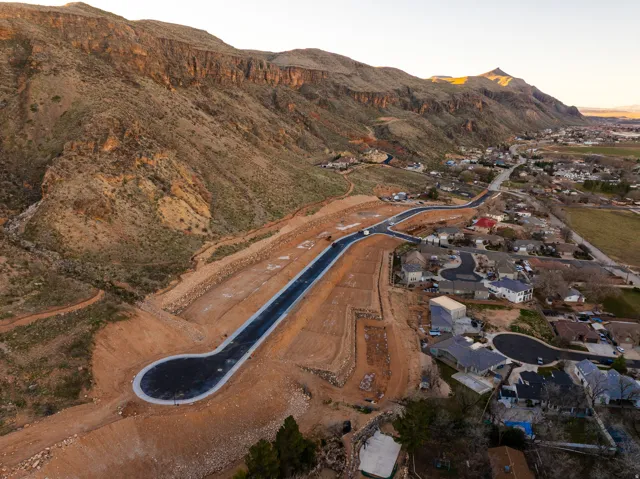 Developing residential area with newly paved roads, surrounded by established homes and natural mountainous terrain