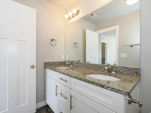 Dual vanity with white cabinetry, granite countertop, and integrated sinks