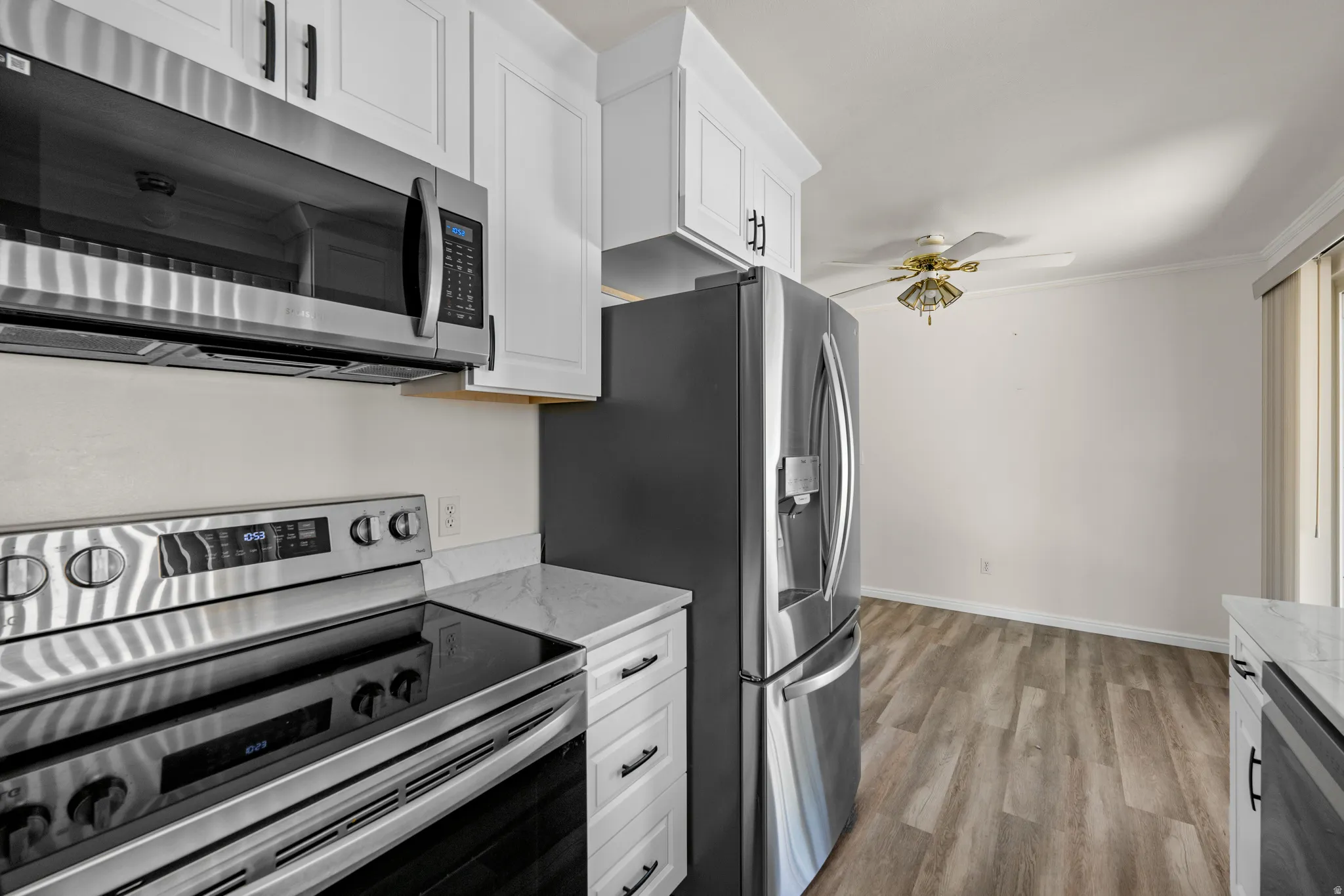 Kitchen featuring stainless steel appliances, white cabinetry with dark hardware, a stone-finish countertop, and wood-finish flooring