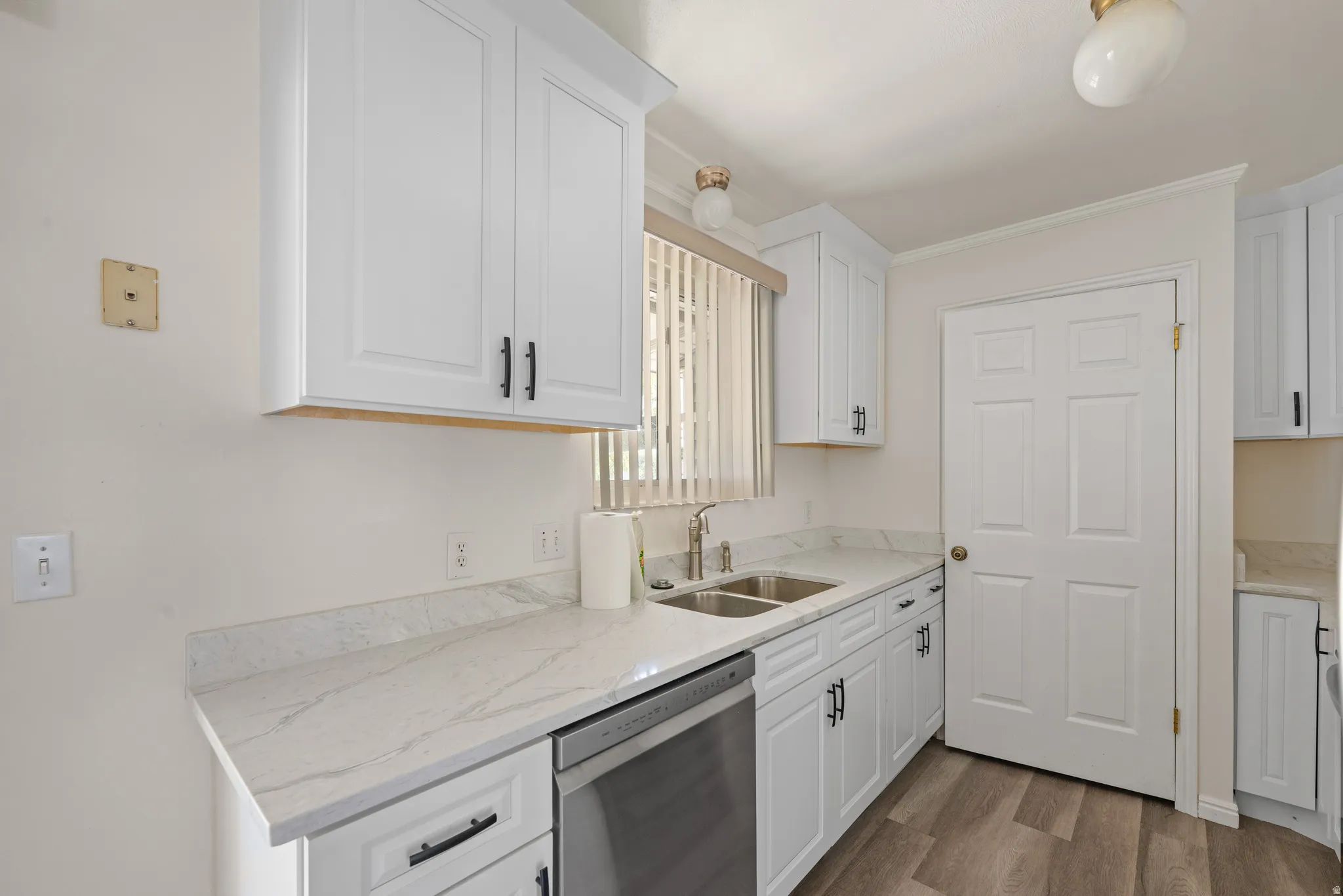 Kitchen featuring white cabinetry, light-toned countertops, a stainless steel sink with a gooseneck faucet, a paneled door, and wood-finish flooring