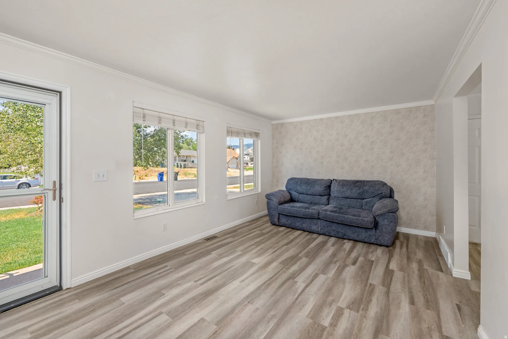 Bright living area featuring wood-finish flooring, a textured accent wall, and multiple windows with blinds