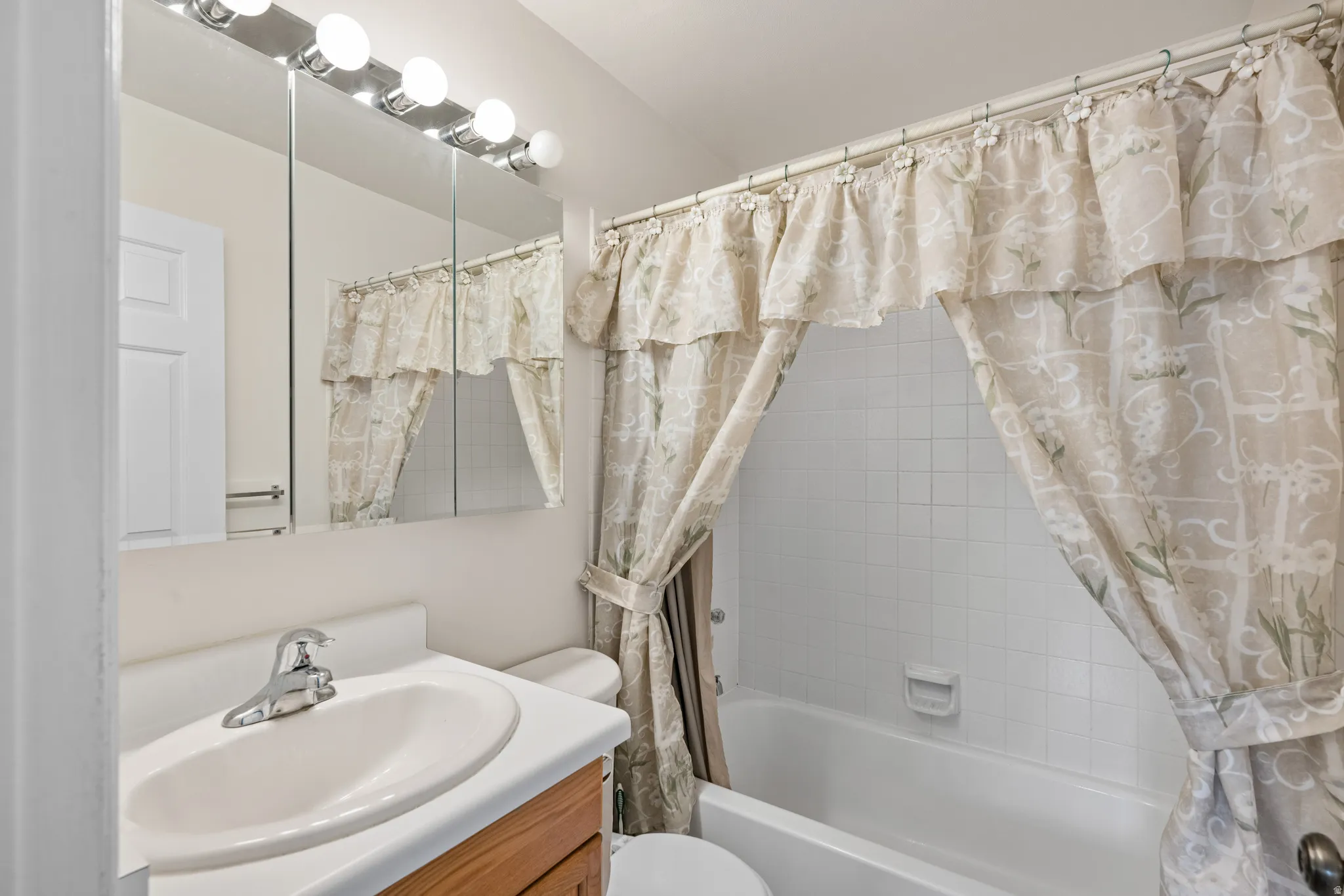 Bathroom featuring a white bathtub, white tile surround, and a wood-finish vanity with an integrated sink