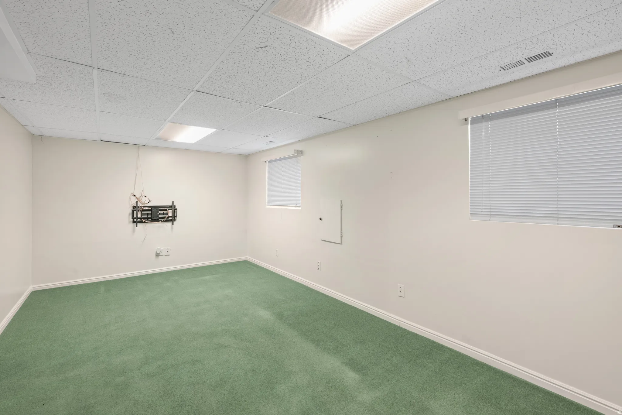 Room featuring green carpeting, neutral wall paint, and a white drop ceiling with integrated lighting