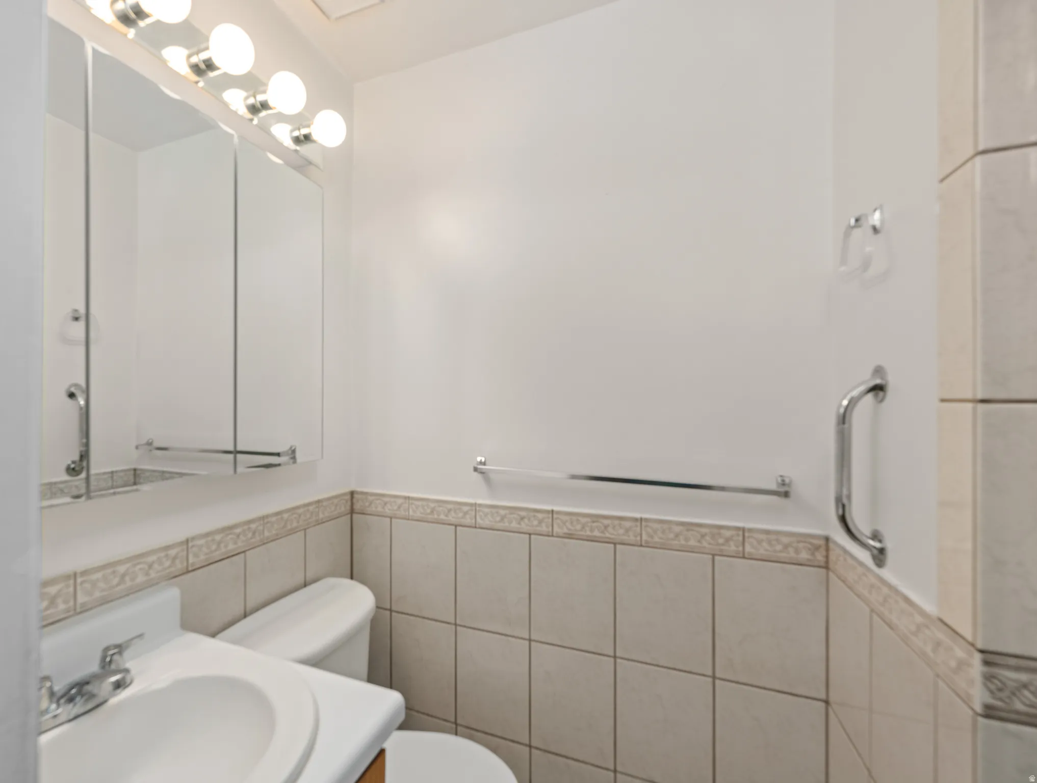 Bathroom featuring a wall-mounted vanity mirror with integrated lighting, a white porcelain sink, and a two-piece toilet