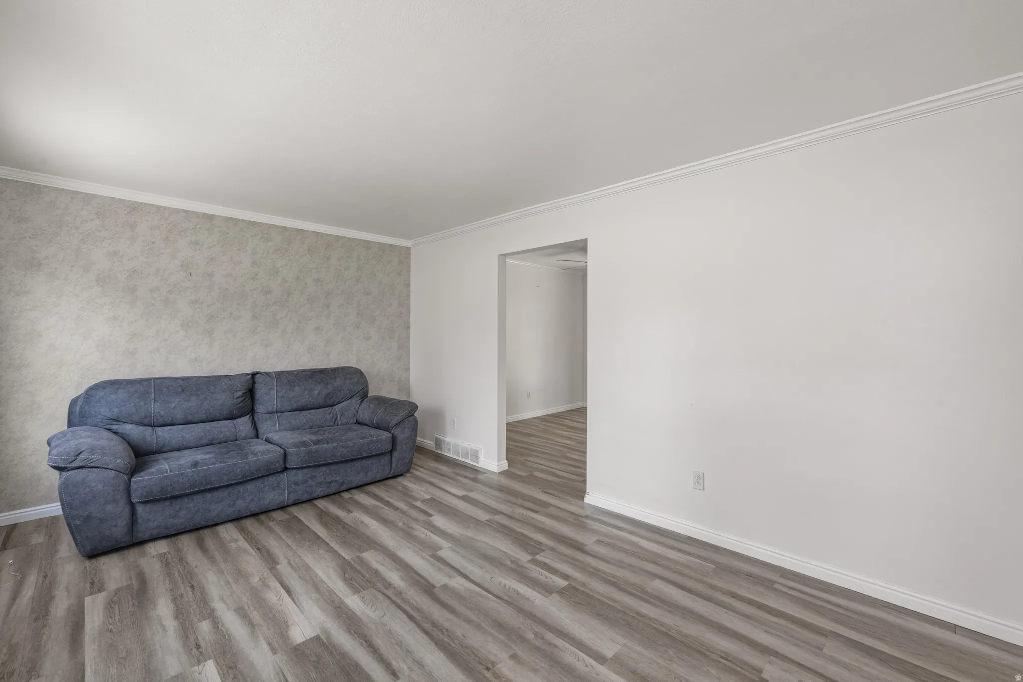 Living area featuring wood-finish flooring, white baseboards, crown molding, and a textured accent wall
