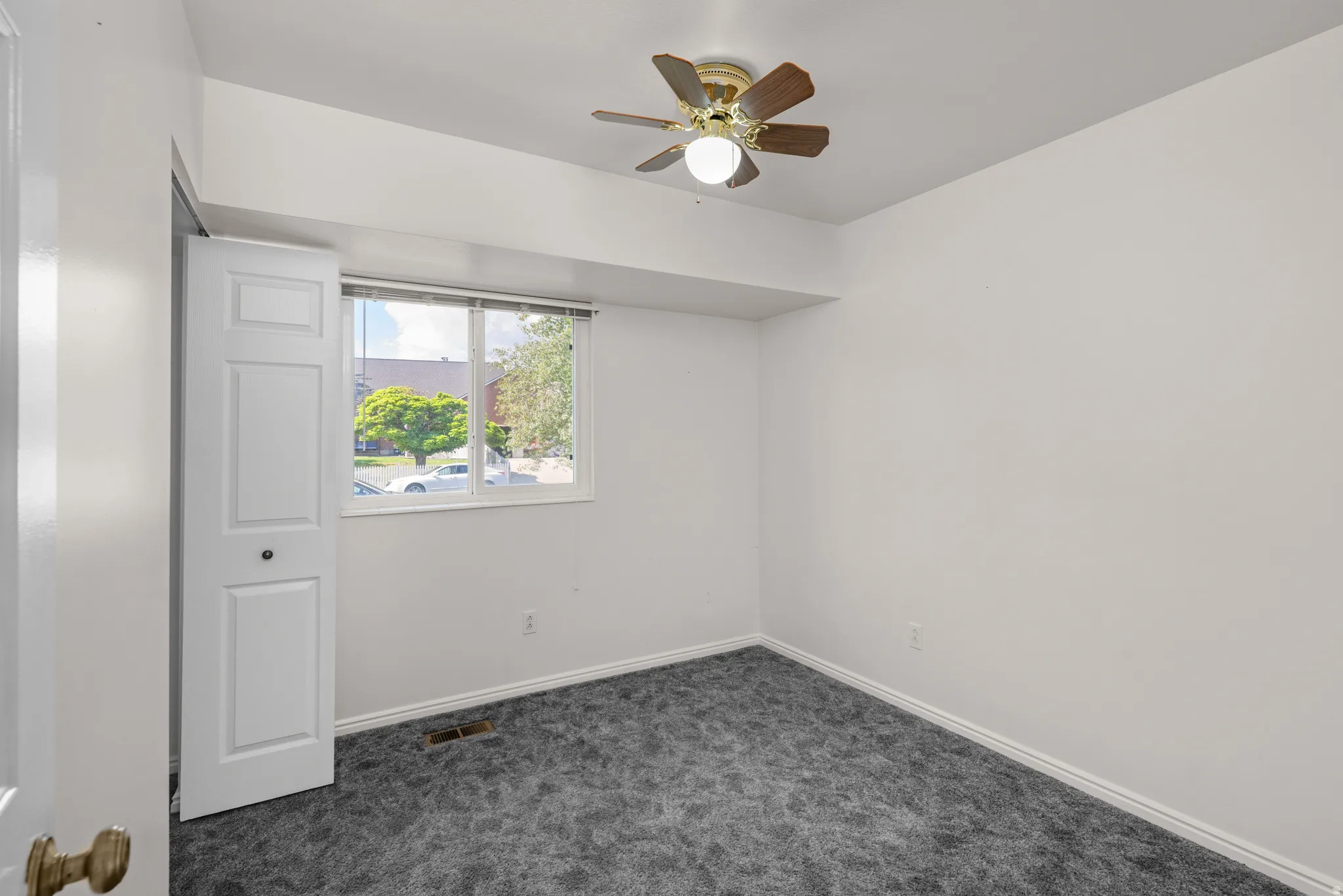 Interior room featuring a ceiling fan with wood-finish blades, a dual-pane window, white baseboards, and dark gray patterned carpeting