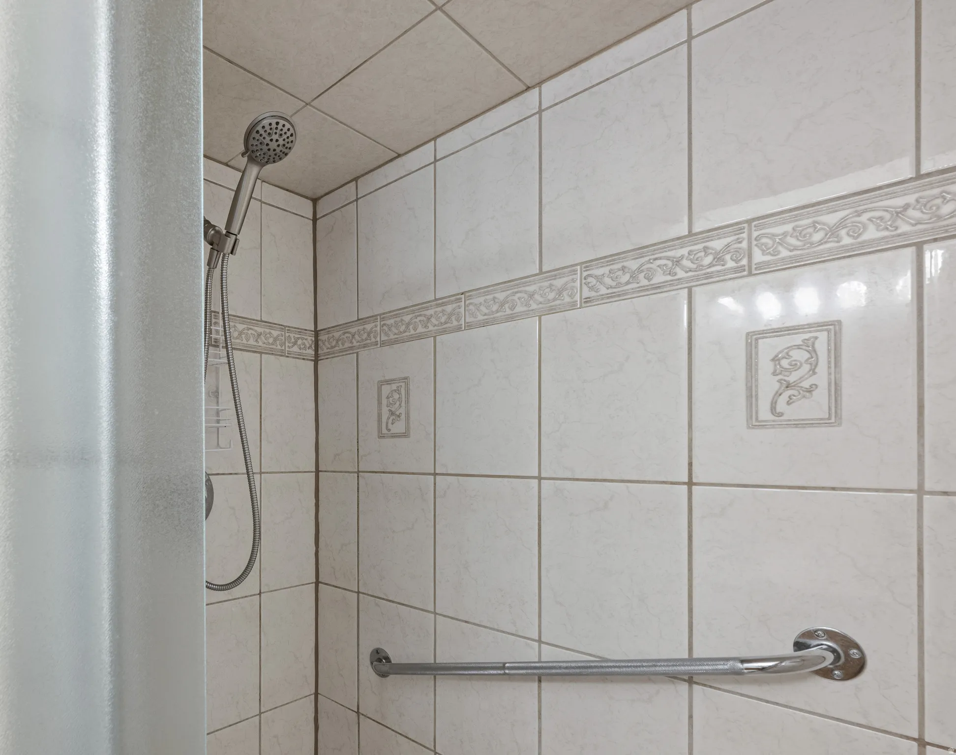 Tiled shower stall featuring a handheld showerhead, decorative accent tiles, and a chrome grab bar