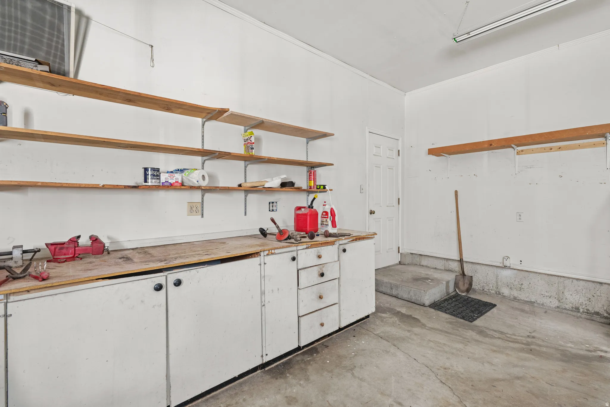 Garage workshop featuring extensive built-in cabinetry, durable concrete flooring, and multiple wood-finish shelving units for organized storage
