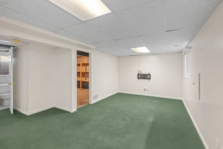 Spacious room featuring green carpeting, white painted walls, and a white acoustical tile ceiling with recessed lighting