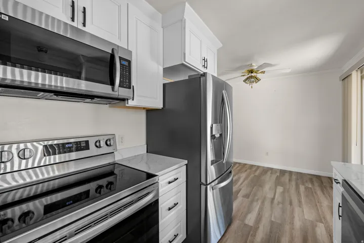 Kitchen featuring stainless steel appliances, white cabinetry with dark hardware, a stone-finish countertop, and wood-finish flooring