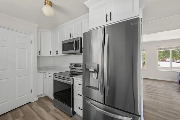 Kitchen featuring white cabinetry, stainless steel appliances, marble-look countertops, and wood-finish flooring