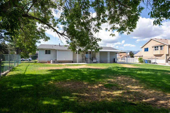 Spacious backyard featuring a manicured lawn, a chain-link fence, and a covered patio area