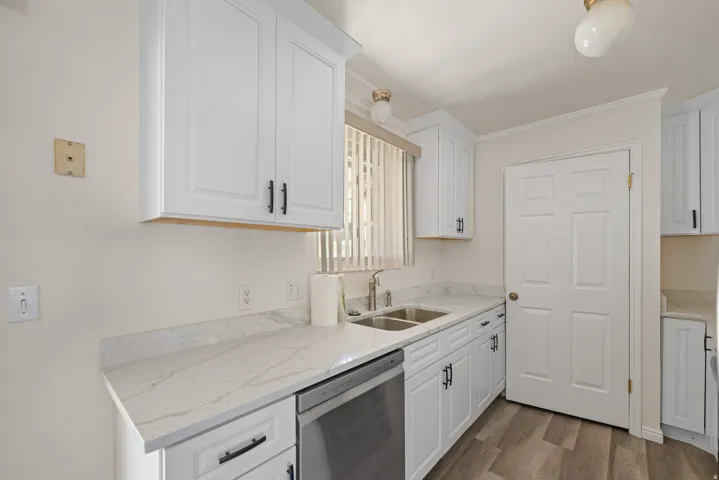 Kitchen featuring white cabinetry, light-toned countertops, a stainless steel sink with a gooseneck faucet, a paneled door, and wood-finish flooring