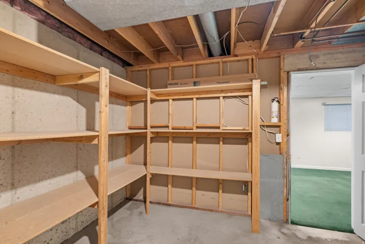 Utility room featuring extensive built-in wooden shelving, exposed ceiling joists, concrete walls, and a concrete floor