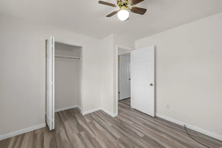 Room featuring wood-finish flooring, a bi-fold closet with hanging rod, a ceiling fan with integrated lighting, and white trim