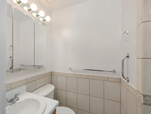Bathroom featuring a wall-mounted vanity mirror with integrated lighting, a white porcelain sink, and a two-piece toilet