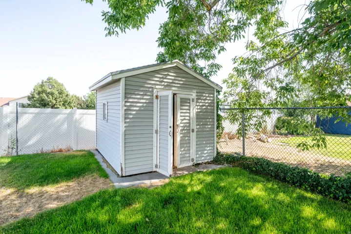 Backyard storage shed with light gray siding, white trim, and double entry doors
