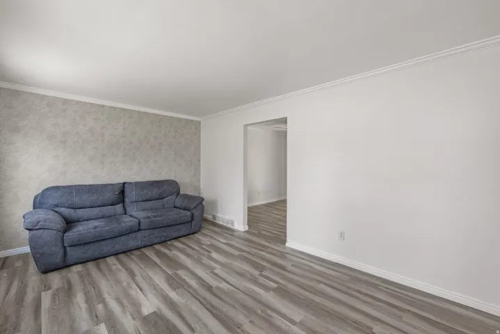 Living area featuring wood-finish flooring, white baseboards, crown molding, and a textured accent wall