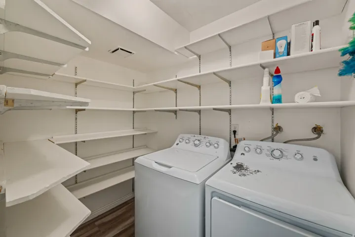 Dedicated laundry area featuring a washer and dryer, extensive built-in shelving, white walls, and wood-finish flooring
