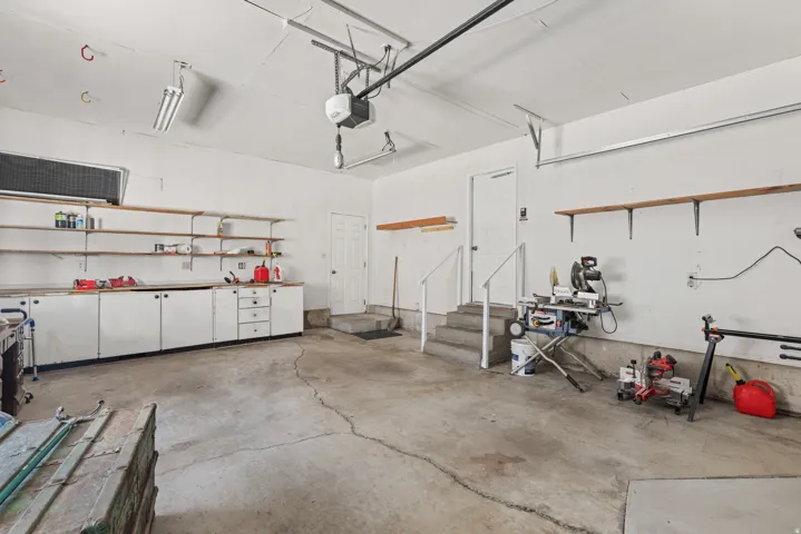 Spacious garage featuring a concrete floor, extensive built-in cabinetry, wall-mounted shelving, overhead lighting, and an automatic garage door opener